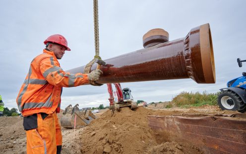 Overwork. Tired man in bright vest taking off his protective helmet and touches face with hand standing near pile of bricks at construction site on fine day
